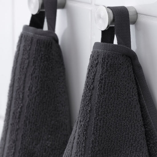 A hand reaching for a folded bath towel on a bathroom shelf.